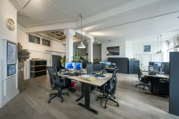 Modern kantoorinterieur aan de De Ruijterkade met open werkplekken, bureaus met computerschermen en natuurlijk licht.